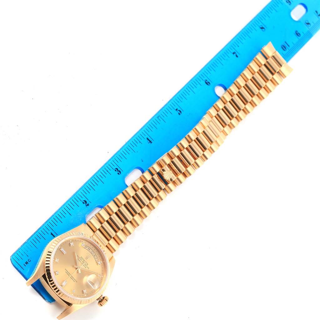 The image shows a President model Rolex watch laying flat against a blue ruler, displaying the watch face and bracelet.
