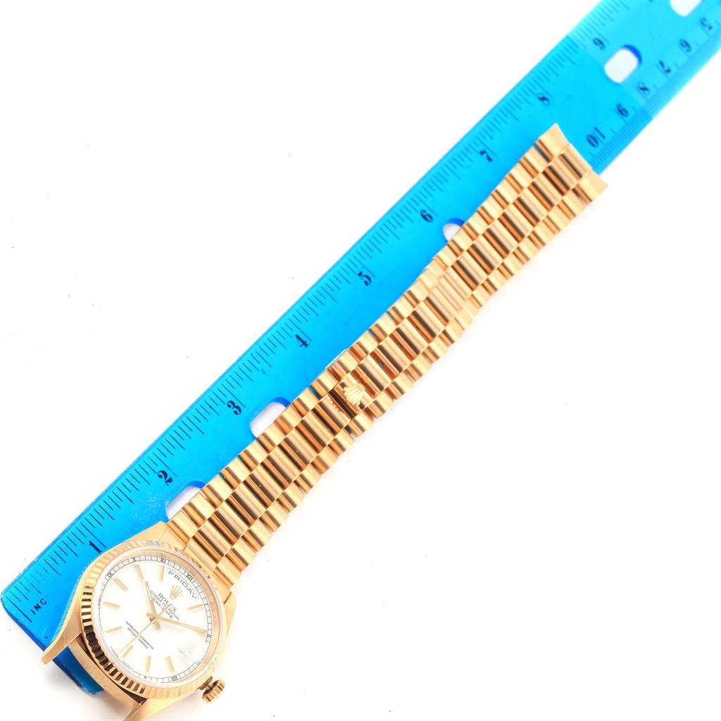 The image shows a top view of a Rolex President 18238 Men
s Yellow Gold White Dial 18238 Men
s Yellow Gold White Dial model watch, including its face and full bracelet, alongside a blue ruler for scale.