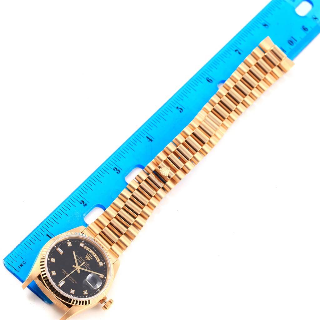 The image shows the President model Rolex watch from an overhead view, highlighting the face, dial, and bracelet against a blue ruler.