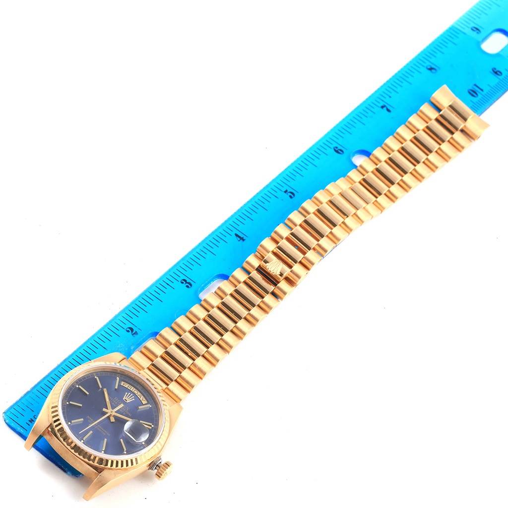 The Rolex President 18038 Men's Yellow Gold Blue Dial 18038 Men's Yellow Gold Blue Dial watch is shown from an overhead angle, with its bracelet aligned along a blue ruler.