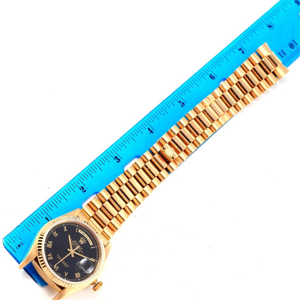 The image shows a Rolex President 18238 Men's Yellow Gold Black Dial 18238 Men's Yellow Gold Black Dial watch model laid flat next to a blue ruler, highlighting its dial and bracelet.