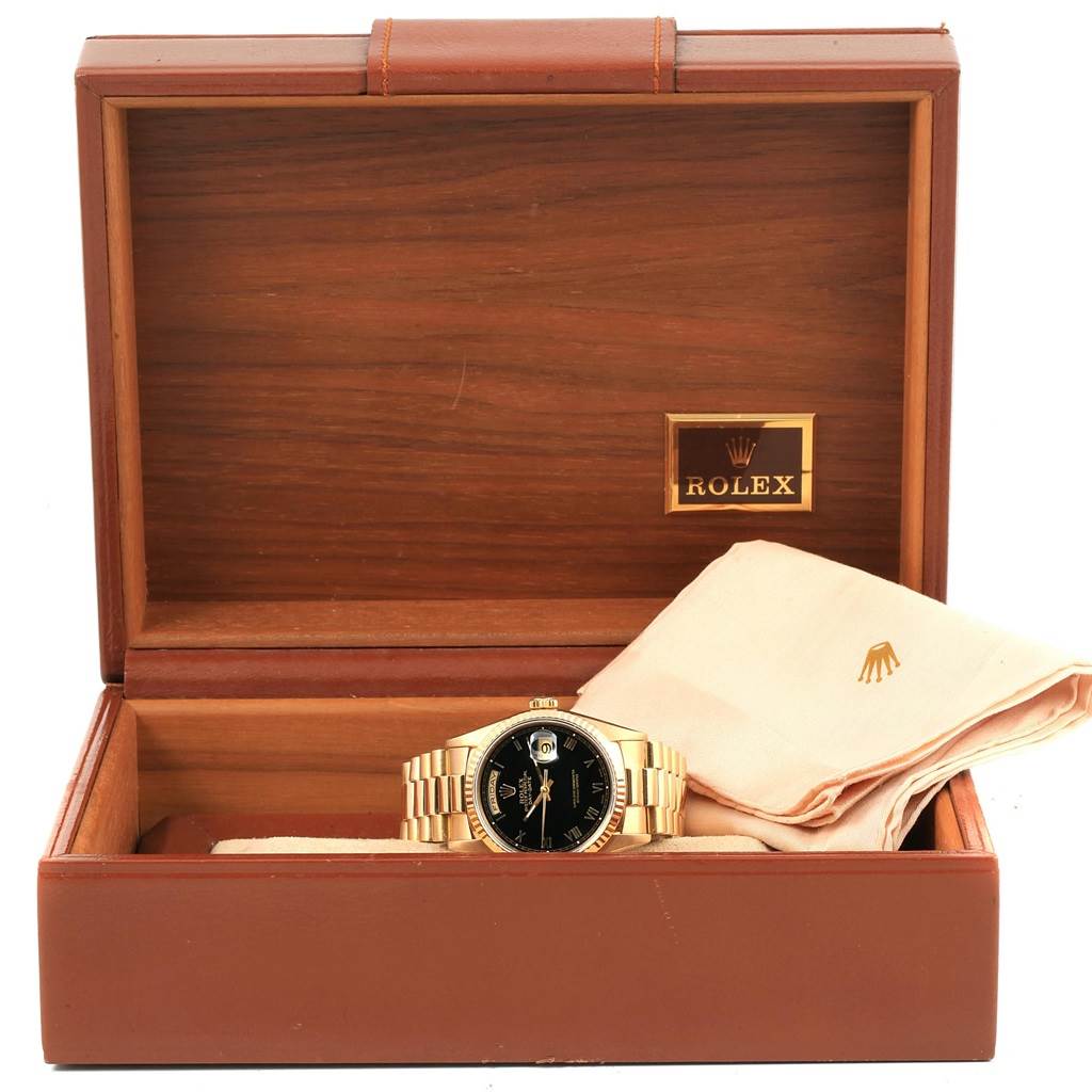 The Rolex President 18238 Men's Yellow Gold Black Dial 18238 Men's Yellow Gold Black Dial model watch is displayed in an open wooden box with a cleaning cloth beside it.