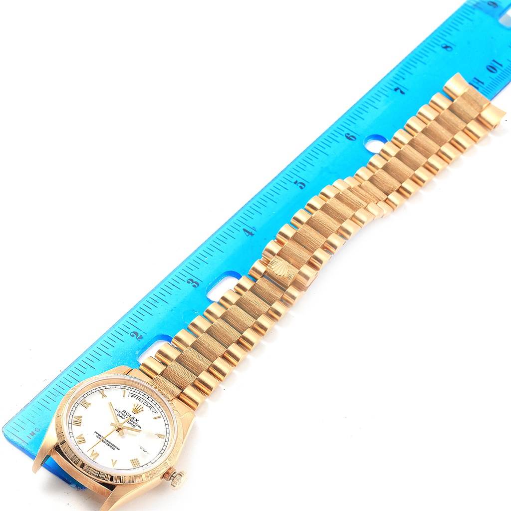 The image shows a Rolex President 18248 Men
s Yellow Gold White Dial 18248 Men
s Yellow Gold White Dial model watch laid flat next to a blue ruler to display its size.