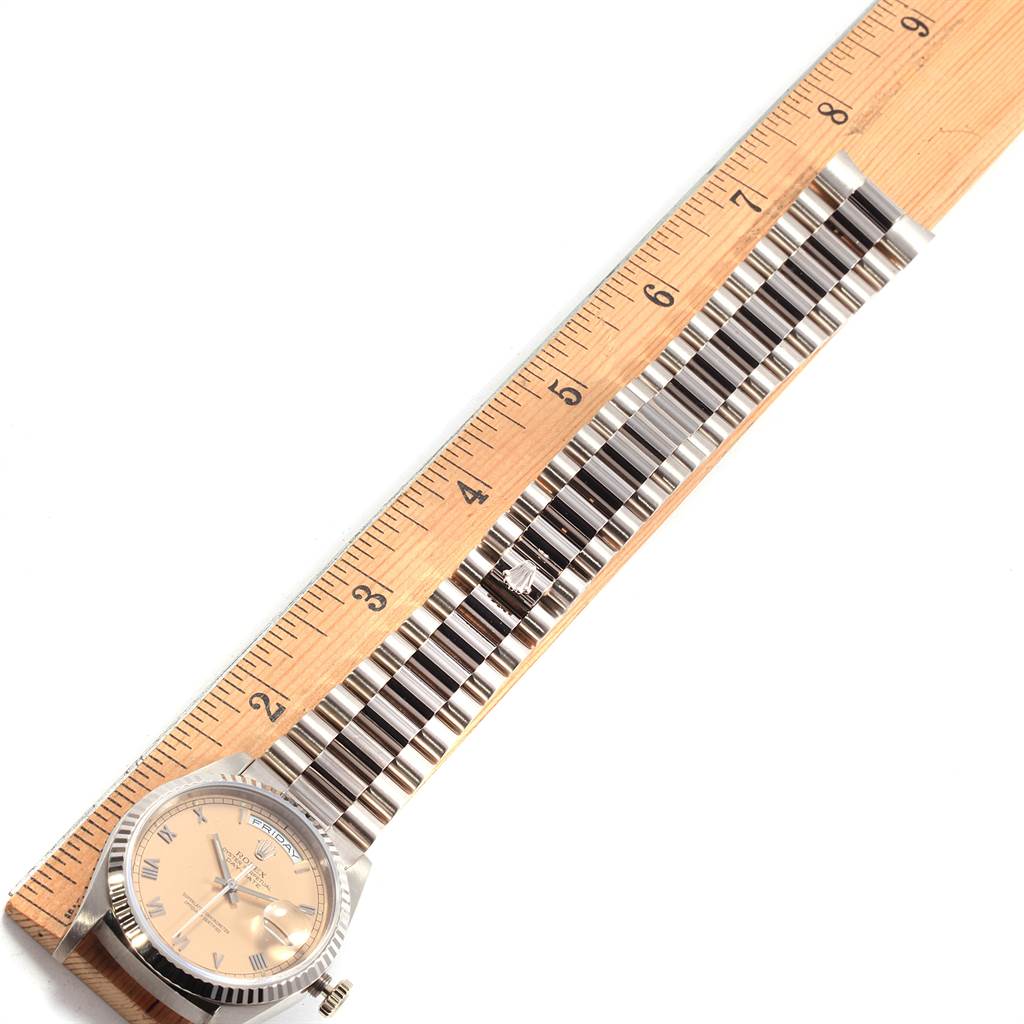 The image shows a top-down view of a Rolex President 18239 Men's White Gold Pink Dial 18239 Men's White Gold Pink Dial model watch next to a wooden ruler, highlighting the watch face and band.
