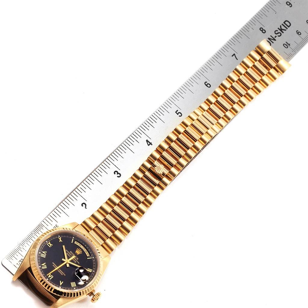 The image shows the front view of a Rolex President 18238 Men
s Yellow Gold Black Dial 18238 Men
s Yellow Gold Black Dial model watch, including the dial, bezel, bracelet, and crown, next to a ruler.