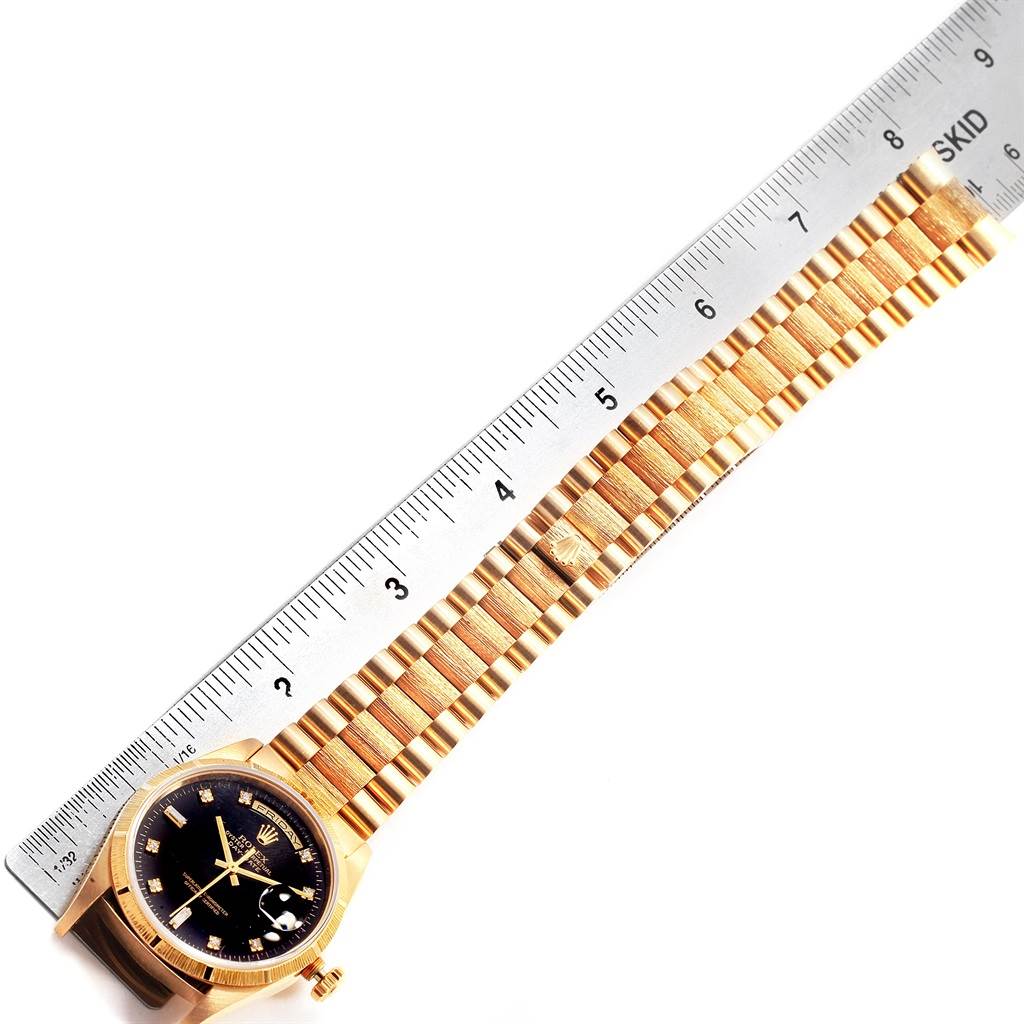 This image shows a Rolex President 18308 Men
s Yellow Gold Black Dial 18308 Men
s Yellow Gold Black Dial model wristwatch laid flat next to a ruler, displaying the face and entire bracelet.