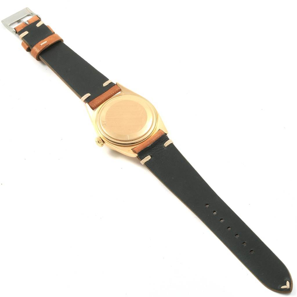 The image shows the backside of a Rolex President 1803 Men
s Yellow Gold Champagne Dial 1803 Men
s Yellow Gold Champagne Dial watch with a gold case and a leather strap.