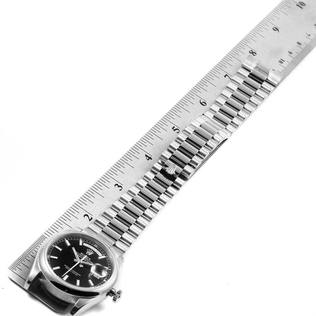 The image shows a side view of a Rolex President 118209 Men's White Gold Black Dial 118209 Men's White Gold Black Dial model watch, focusing on its face, crown, and bracelet next to a ruler for scale.