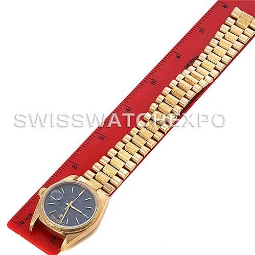 This image shows a gold Rolex President 18038 Men's Yellow Gold Blue Dial 18038 Men's Yellow Gold Blue Dial model watch laying flat on a red ruler, displaying both the dial and bracelet. 
