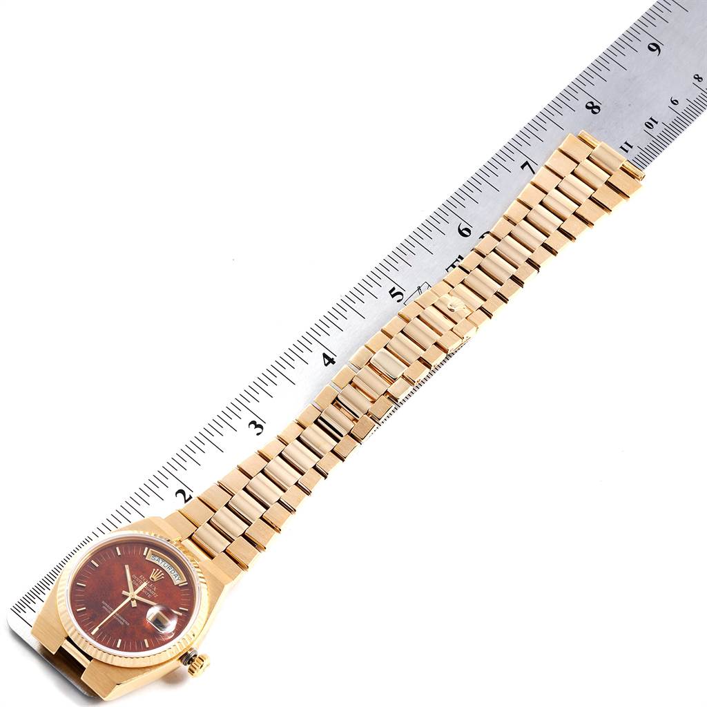 The image shows a Rolex President 14418 Men
s Yellow Gold Brown Dial 14418 Men
s Yellow Gold Brown Dial model watch laid flat next to a ruler, displaying its full band and maroon watch face.
