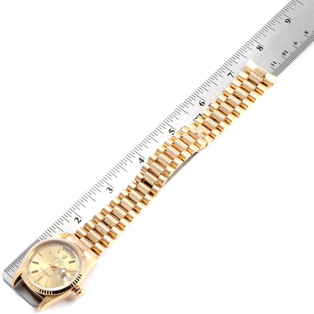 A Rolex President 18238 Men
s Yellow Gold Champagne Dial 18238 Men
s Yellow Gold Champagne Dial watch is shown from an overhead angle with its band extended alongside a ruler.