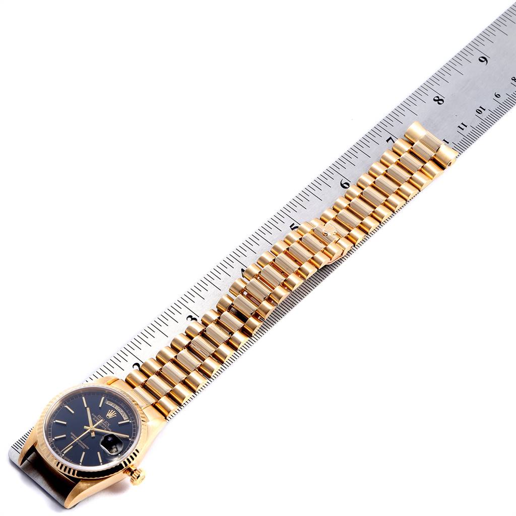 The Rolex President 18238 Men
s Yellow Gold Black Dial 18238 Men
s Yellow Gold Black Dial model watch is shown flat with its gold bracelet aligned against a ruler for measurement.