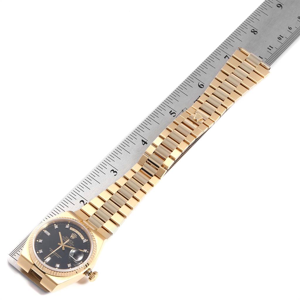 The image shows a Rolex President 19018 Men
s Yellow Gold Black Dial 19018 Men
s Yellow Gold Black Dial model watch lying flat with its band and face alongside a ruler for scale.