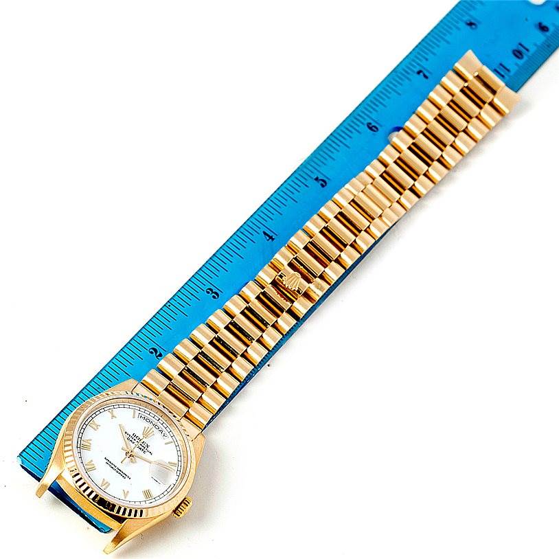 The image shows a Rolex President 18238 Men's Yellow Gold White Dial 18238 Men's Yellow Gold White Dial model watch laid flat against a blue ruler, displaying its face and gold link bracelet.