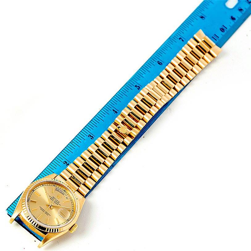 The image shows a gold Rolex President 18238 Men
s Yellow Gold Champagne Dial 18238 Men
s Yellow Gold Champagne Dial watch laid flat next to a blue ruler, showcasing the face and full bracelet.