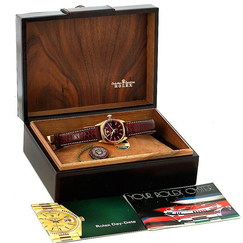 The image shows a Rolex President 18038 Men
s Yellow Gold Champagne Dial 18038 Men
s Yellow Gold Champagne Dial watch in a wooden box, with a burgundy leather strap, and includes booklets and a tag.