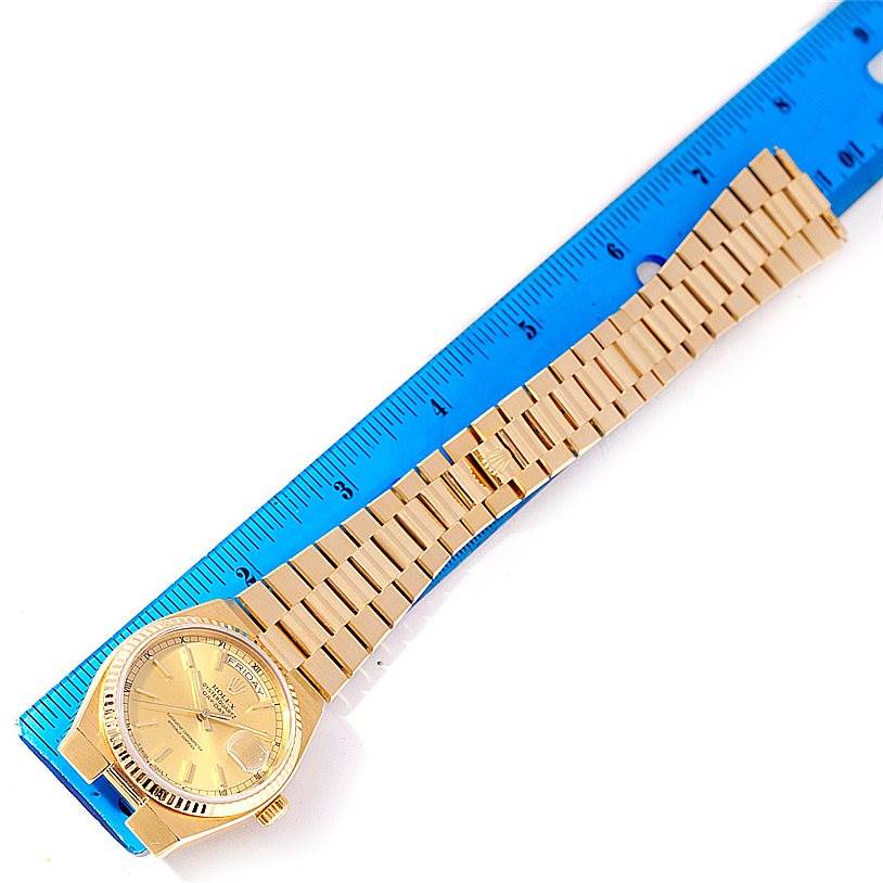 The image shows a Rolex President 19000 Men
s Yellow Gold Champagne Dial 19000 Men
s Yellow Gold Champagne Dial model watch laid flat alongside a blue ruler, displaying the watch face and band.