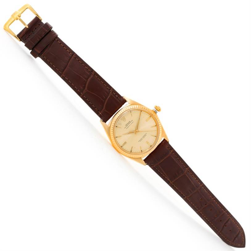 The image shows a Rolex President 1013 Men
s Yellow Gold Champagne Dial 1013 Men
s Yellow Gold Champagne Dial model watch, viewed from above, featuring a brown leather strap and a gold case with a beige dial.