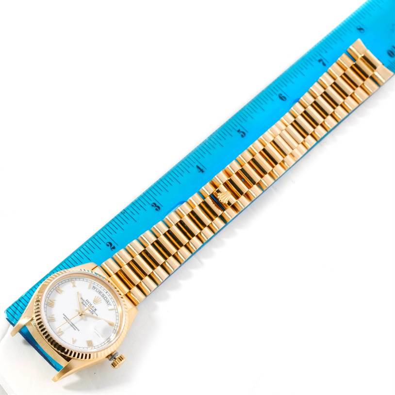 The image shows a Rolex President 18038 Men
s Yellow Gold White Dial 18038 Men
s Yellow Gold White Dial model watch from a top-down angle, including the face, bezel, and bracelet next to a ruler.