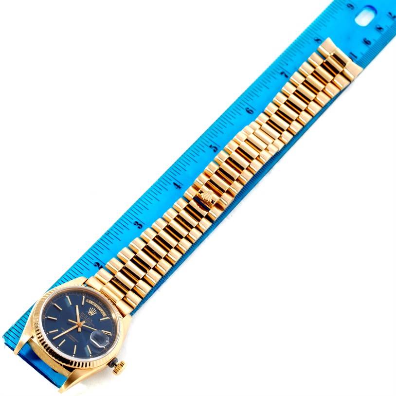 The image shows a horizontal view of a Rolex President 18038 Men's Yellow Gold Blue Dial 18038 Men's Yellow Gold Blue Dial model watch with its face, bezel, and bracelet placed on a blue ruler.