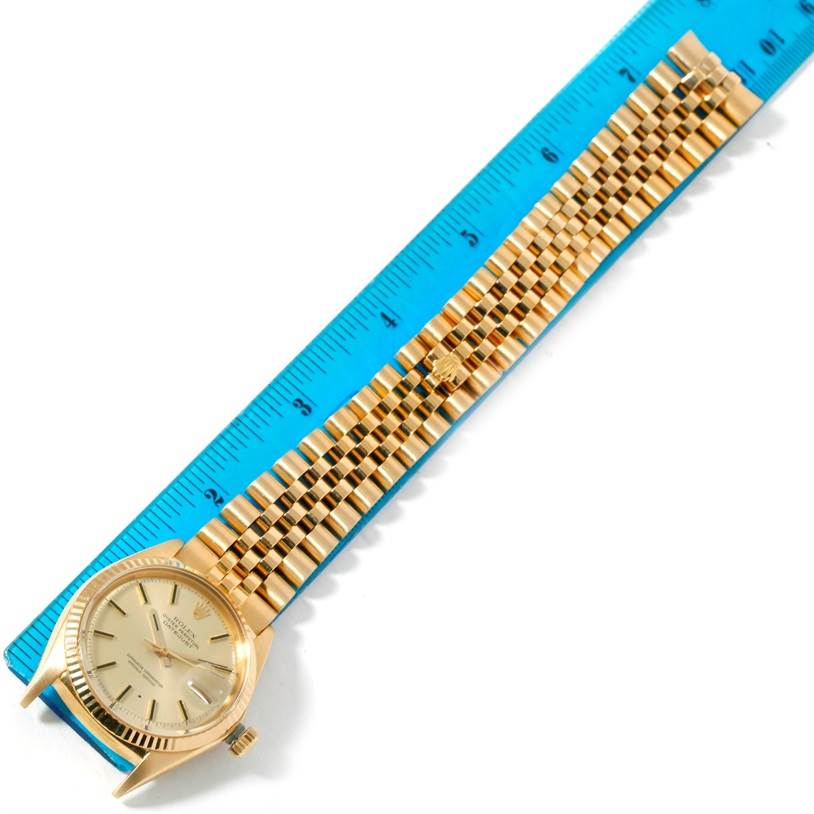 The image shows a Rolex President 1601 Men
s Yellow Gold Champagne Dial 1601 Men
s Yellow Gold Champagne Dial model watch lying flat next to a blue ruler, displaying the watch face and full bracelet.