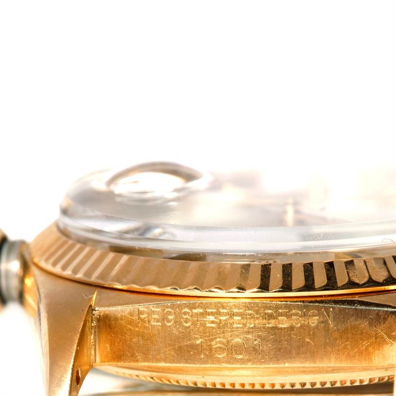 The image shows a close-up side angle of a Rolex President 1601 Men
s Yellow Gold Champagne Dial 1601 Men
s Yellow Gold Champagne Dial model watch, featuring the fluted bezel and part of the case with engravings.