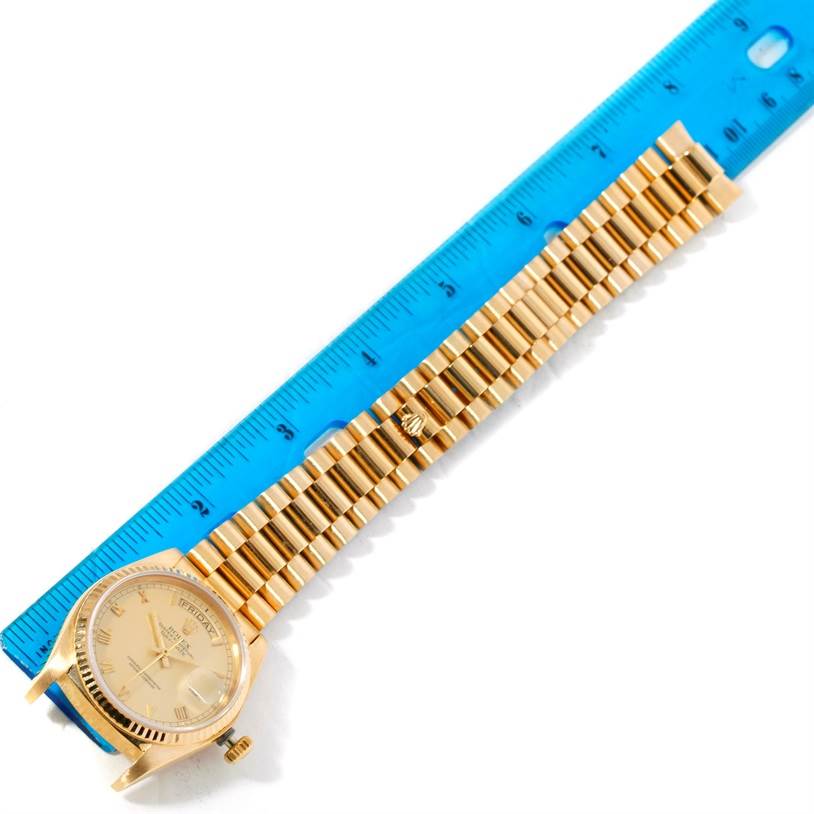 The image displays a Rolex President 18038 Men
s Yellow Gold Champagne Dial 18038 Men
s Yellow Gold Champagne Dial watch with its gold bracelet placed beside a blue ruler, viewed from above.