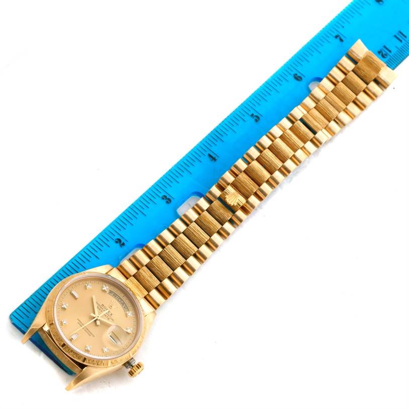 The image shows a top-down view of a Rolex President 18078 Men
s Yellow Gold Champagne Dial 18078 Men
s Yellow Gold Champagne Dial model watch, including its face, case, and band, next to a blue ruler.