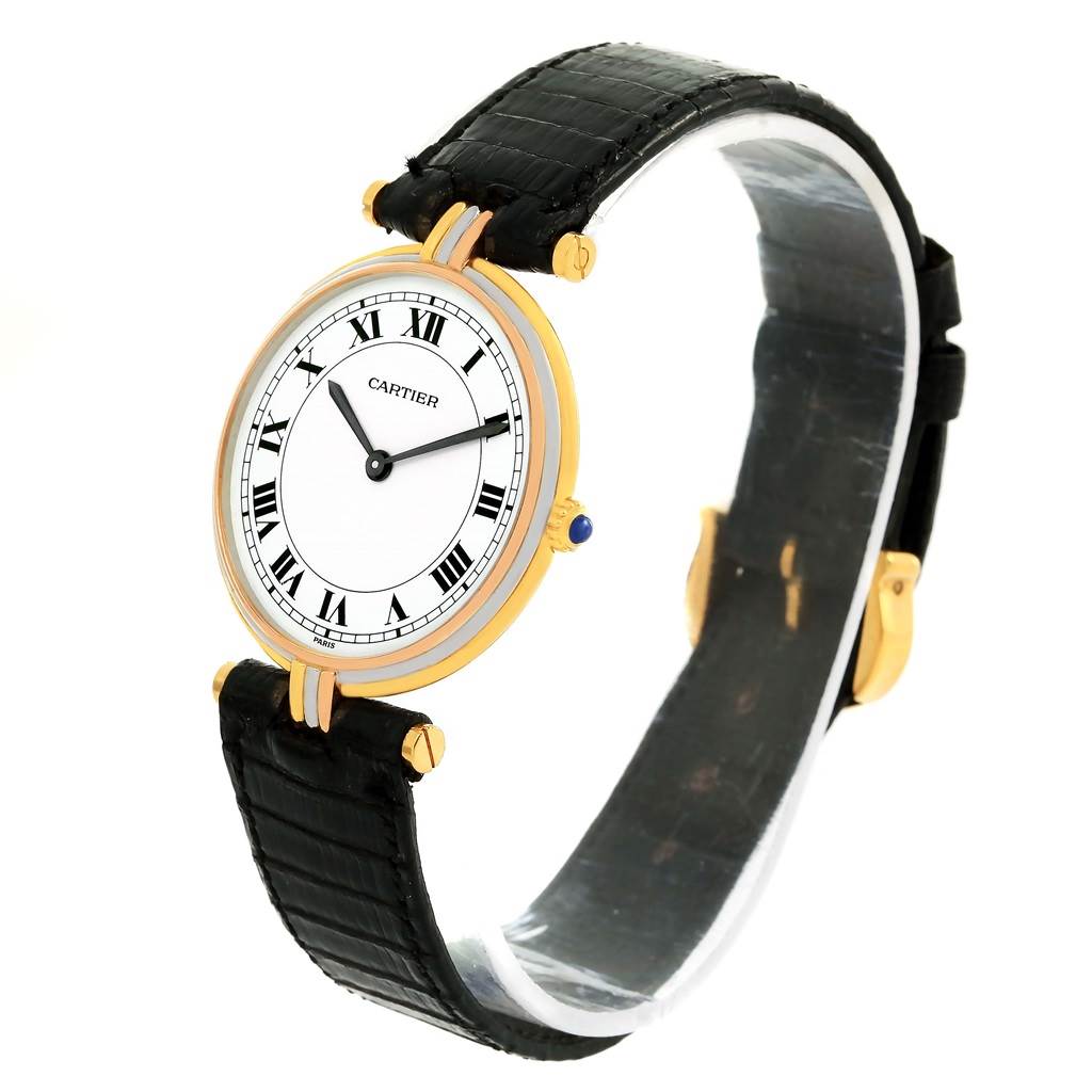 The image shows a Cartier Trinity W1514457 Yellow Gold White Dial W1514457 Yellow Gold White Dial model watch at a three-quarter angle, highlighting its face, bezel, and black leather strap.