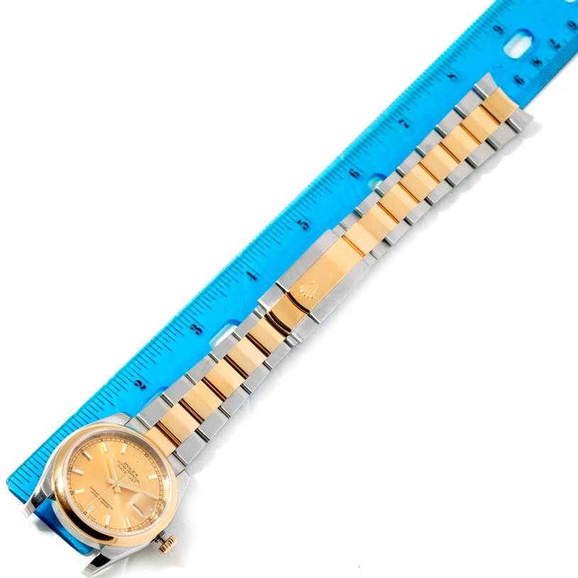 The image shows a top-down view of a Rolex Datejust 116203 Men
s Stainless Steel Champagne Dial 116203 Men
s Stainless Steel Champagne Dial watch, displaying the face, bezel, and two-tone bracelet next to a blue ruler.