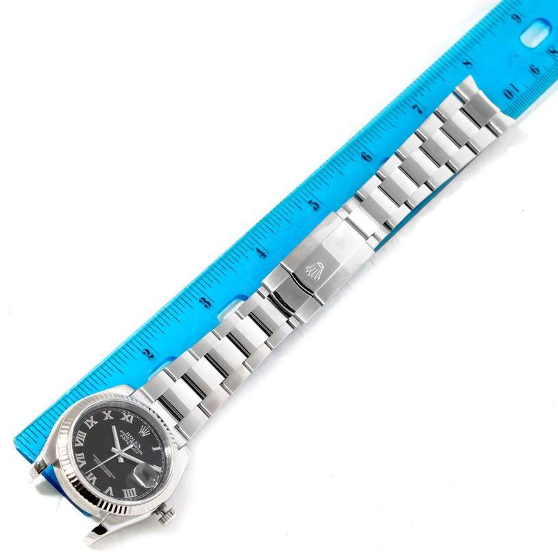 The Rolex Datejust 116234 Men
s Stainless Steel Black Dial 116234 Men
s Stainless Steel Black Dial watch is shown from a top-down angle, highlighting its dial, bezel, and bracelet, with a ruler for scale.