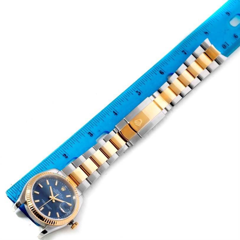 The image shows a Rolex Datejust 116233 Men's Stainless Steel Blue Dial 116233 Men's Stainless Steel Blue Dial watch laid next to a ruler, highlighting the face, bezel, and part of the metal bracelet.