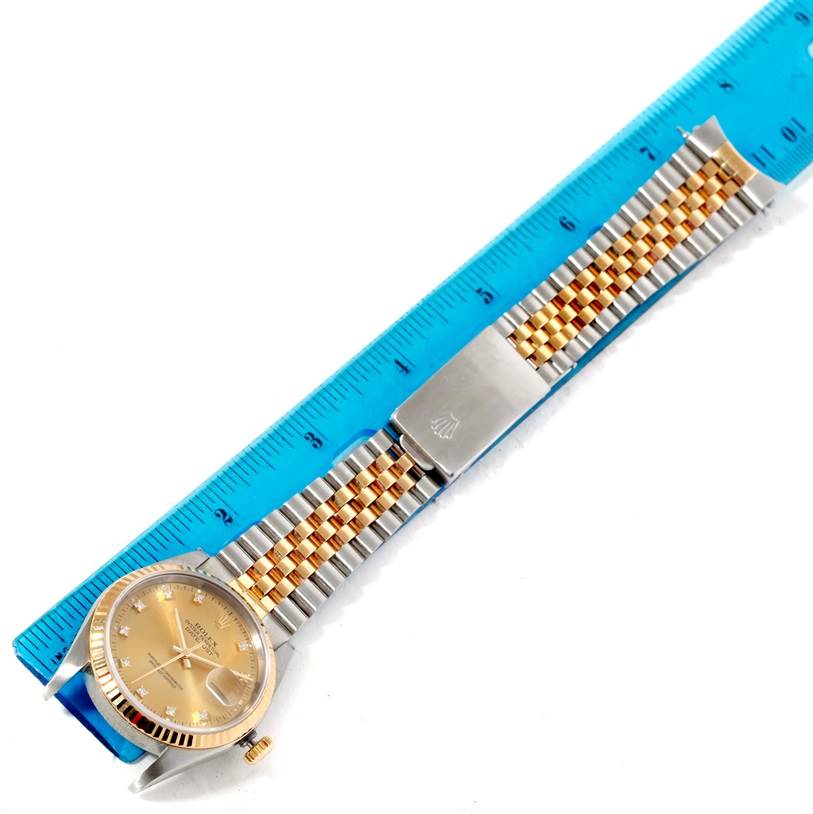 The Rolex Datejust 16233 Men's Steel and Gold (two tone) Champagne Dial 16233 Men's Steel and Gold (two tone) Champagne Dial watch is shown from a top-down angle, featuring its face, bezel, and jubilee bracelet beside a blue ruler.