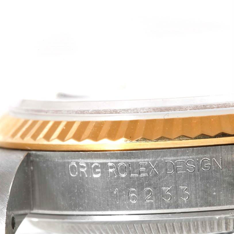 The image shows a close-up of the side of a Rolex Datejust 16233 Men
s Steel and Gold (two tone) White Dial 16233 Men
s Steel and Gold (two tone) White Dial watch, featuring its fluted bezel and engraved case with the model number 16233.