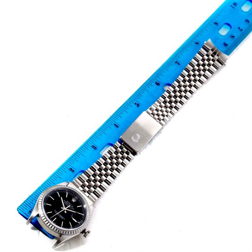 The Rolex Datejust 16220 Men
s Stainless Steel Black Dial 16220 Men
s Stainless Steel Black Dial watch is shown laying flat with its full bracelet and clasp visible, alongside a blue ruler.