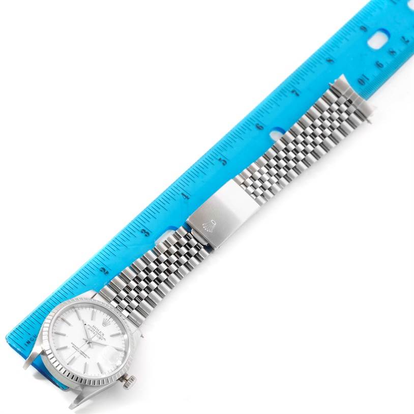 The image shows a Rolex Datejust 16220 Men
s Stainless Steel White Dial 16220 Men
s Stainless Steel White Dial watch lying flat with its silver dial, fluted bezel, and Jubilee bracelet alongside a blue ruler.