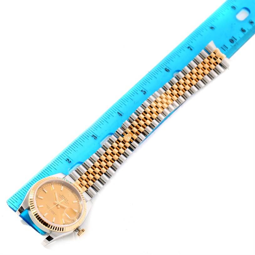 The Rolex Datejust 116233 Men's Stainless Steel Champagne Dial 116233 Men's Stainless Steel Champagne Dial watch is shown from a top-down angle, highlighting its dial, case, and two-tone bracelet against a ruler.