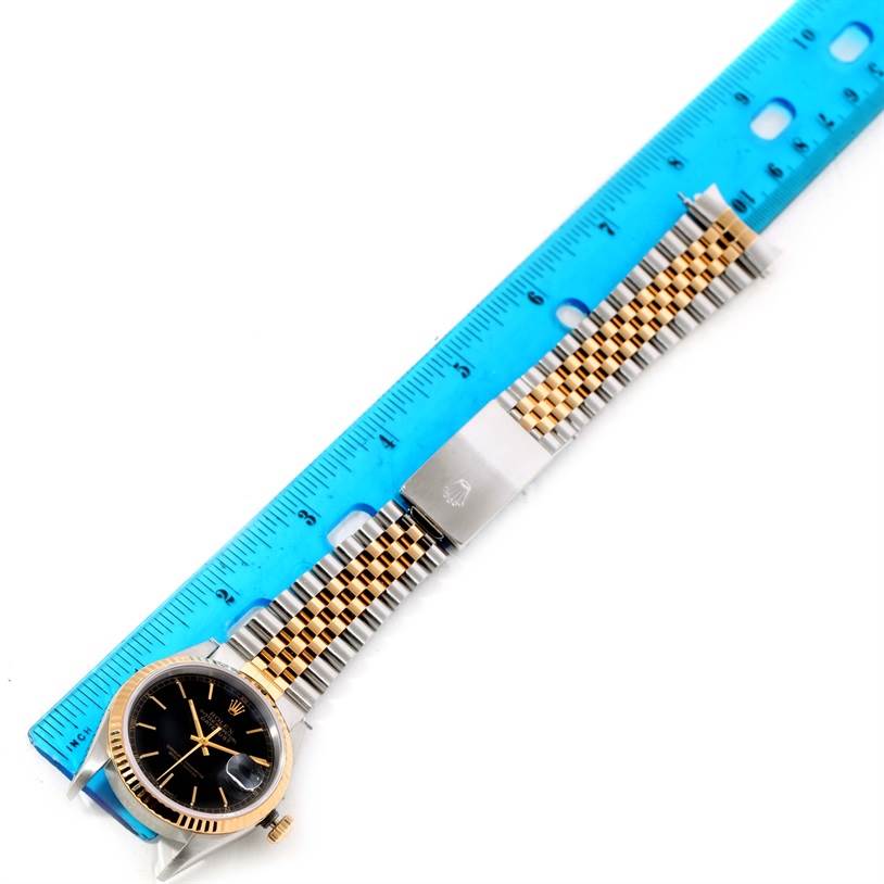 The image shows a Rolex Datejust 16233 Men's Steel and Gold (two tone) Black Dial 16233 Men's Steel and Gold (two tone) Black Dial watch with a two-tone bracelet next to a blue ruler for measurement, captured from above.