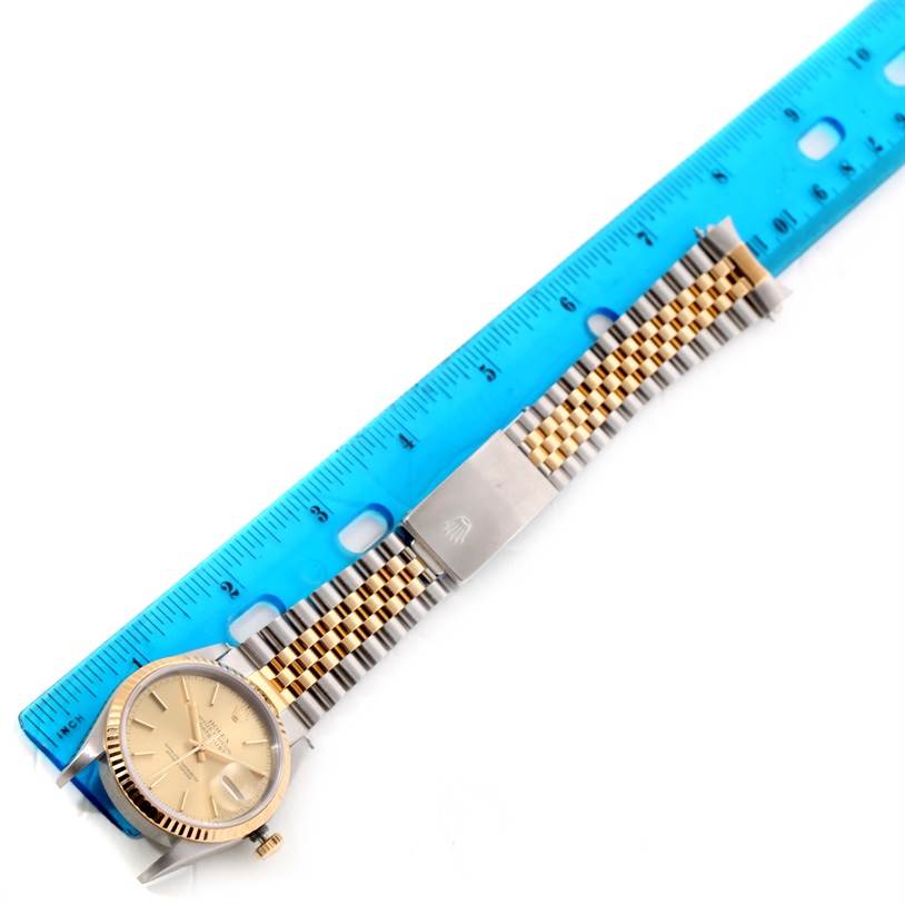 The image shows a top-down view of a Rolex Datejust 16233 Men's Steel and Gold (two tone) Champagne Dial 16233 Men's Steel and Gold (two tone) Champagne Dial watch, highlighting its dial, bezel, and two-tone bracelet against a blue ruler.