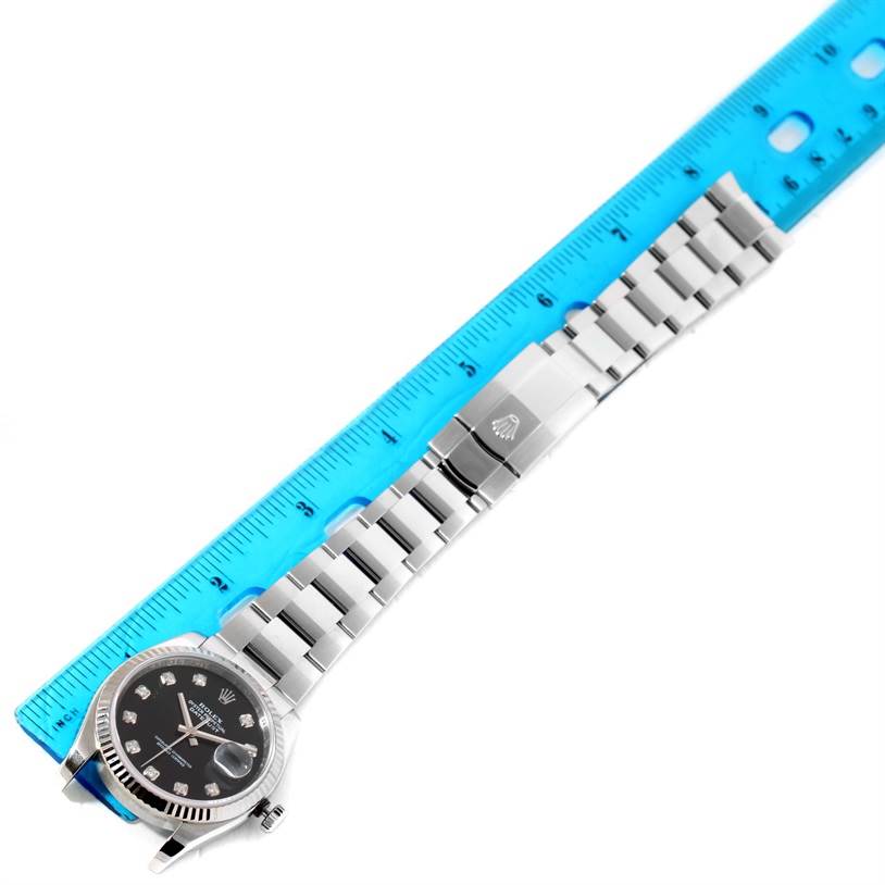 The image displays a Rolex Datejust 116234BKDO Men's Stainless Steel Silver Dial 116234BKDO Men's Stainless Steel Silver Dial watch laid flat with a blue ruler alongside, showcasing the face, bracelet, and clasp.