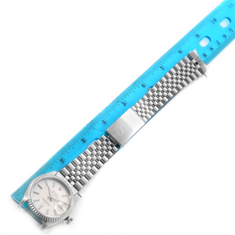 The image shows the Rolex Datejust 16220 Men's Stainless Steel Silver Dial 16220 Men's Stainless Steel Silver Dial watch with its full stainless steel band, placed alongside a blue measuring ruler.