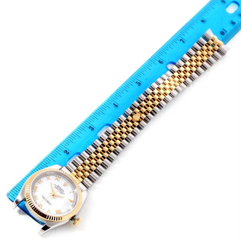 The image shows a Rolex Datejust 116233 Men
s Stainless Steel White Dial 116233 Men
s Stainless Steel White Dial watch partially side-viewed, with its face and band laid against a blue ruler.