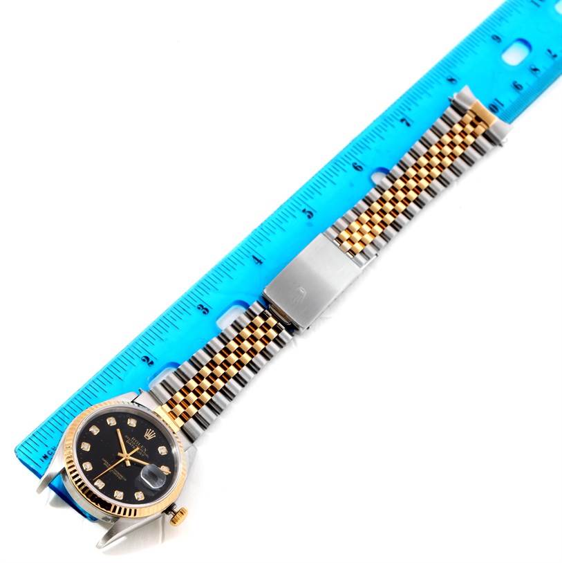 The Rolex Datejust 16233 Men's Steel and Gold (two tone) Black Dial 16233 Men's Steel and Gold (two tone) Black Dial watch is shown from an overhead angle, featuring its black dial, case, and two-tone bracelet next to a ruler.