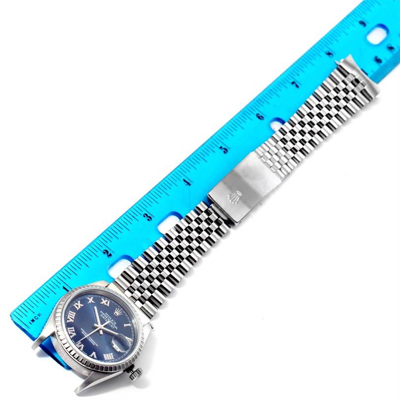 The image shows a Rolex Datejust 16220 Men's Stainless Steel Blue Dial 16220 Men's Stainless Steel Blue Dial watch and part of its jubilee bracelet, with a blue dial and Roman numerals, next to a ruler.