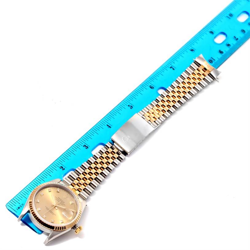 The Rolex Datejust 16233 Men's Steel and Gold (two tone) Champagne Dial 16233 Men's Steel and Gold (two tone) Champagne Dial watch is shown from a top view, displaying the face, bracelet, and clasp alongside a blue ruler.