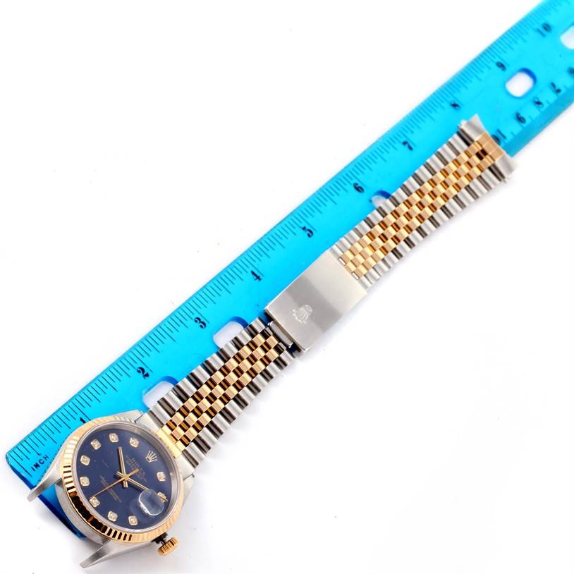 The Rolex Datejust 16233 Men's Steel and Gold (two tone) Blue Dial 16233 Men's Steel and Gold (two tone) Blue Dial watch is shown flat with its face, bracelet, and clasp, next to a blue ruler for scale.