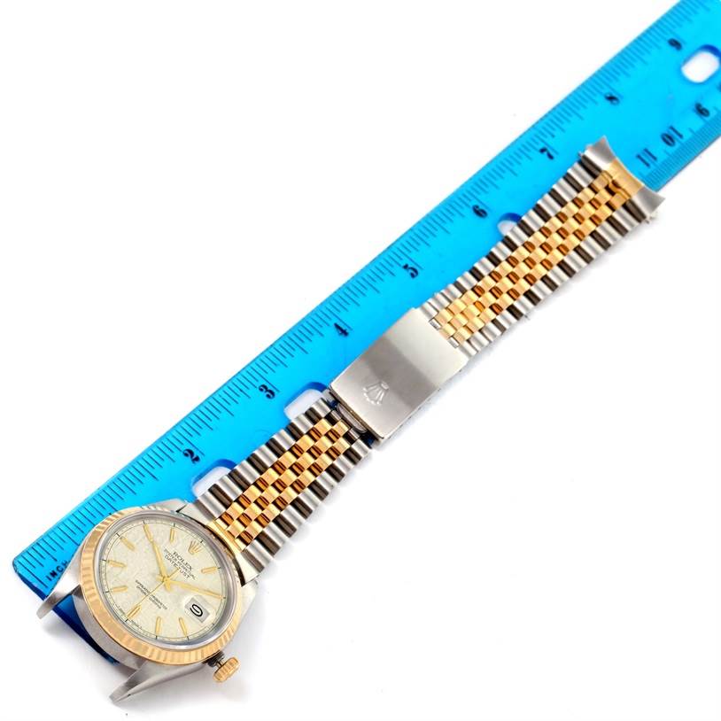 The image shows a Rolex Datejust 16233 Men's Steel and Gold (two tone) Beige Dial 16233 Men's Steel and Gold (two tone) Beige Dial watch placed horizontally next to a blue ruler, highlighting its gold and silver jubilee bracelet.