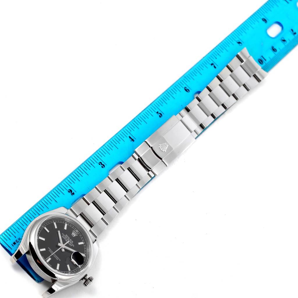 The Rolex Datejust 116200 Men's Stainless Steel Black Dial 116200 Men's Stainless Steel Black Dial watch is shown at a flat angle, featuring the dial, bracelet, and clasp next to a blue ruler.