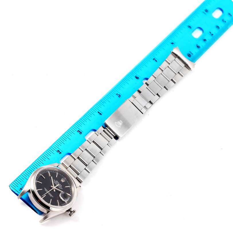 The image shows a top-down view of a Rolex Datejust 16200 Men
s Stainless Steel Black Dial 16200 Men
s Stainless Steel Black Dial watch, including the face and entire metal band, with a blue ruler for scale.