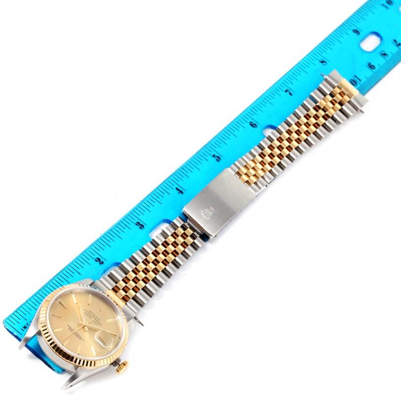 This image shows a Rolex Datejust 16233 Men's Steel and Gold (two tone) Champagne Dial 16233 Men's Steel and Gold (two tone) Champagne Dial watch laid flat, highlighting the closed stainless steel and gold bracelet with a blue ruler for scale.